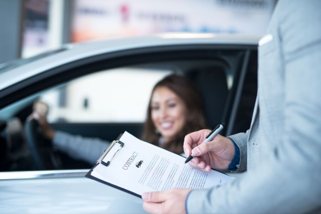 Close-up of a contract being signed,after the customer learned about the tips for choosing the right car , on a clipboard next to a rental car, with the smiling customer seated in the driver's seat.