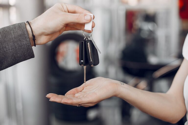 Close-up of a person handing a set of black car keys and a remote fob to a customer at a rental or dealership desk.